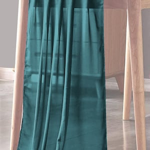 May include: Teal blue table runner made of sheer fabric, draped over a wooden table.