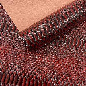 May include: A close-up of red faux leather with a glossy, snake-skin texture. The material is rolled up, revealing a smooth, peach-colored backing. The surface reflects light, highlighting the scales.