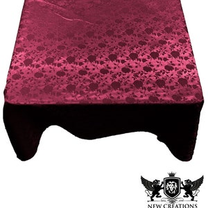 May include: A burgundy table cloth with a floral pattern. The tablecloth is made of a satin-like material and has a slight sheen.
