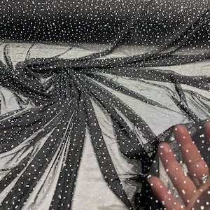 May include: Black mesh fabric with scattered, sparkling rhinestones. The fabric is draped, showing folds and texture. The rhinestones are various sizes and reflect light, creating a shimmering effect. Ideal for apparel and craft projects.