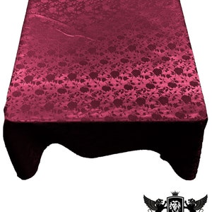 May include: A burgundy satin tablecloth with a rose pattern. The tablecloth is draped over a table and has a slight sheen.