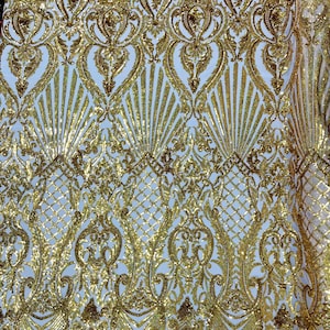 Puede incluir: Tela de lentejuelas doradas con un patrón de damasco. La tela tiene un respaldo de malla transparente.