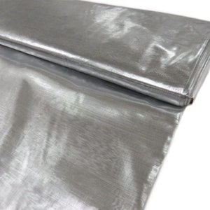 Könnte beinhalten: Silberner Metallic-Stoff mit einem dezenten Glanz. Der Stoff ist in der Mitte gefaltet und zeigt die Textur und den Schimmer.