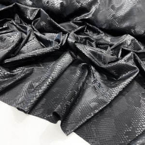 May include: Black faux leather fabric with a snakeskin pattern. The fabric is wrinkled and folded.