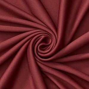 Könnte beinhalten: Ein tiefburgunderroter Stoff mit einer glatten, matten Textur. Das Material ist in einem zentralen Spiralwirbel angeordnet, wodurch weiche, strahlenförmige Falten und Schatten entstehen, die die gleichmäßige, dunkelrote Farbe betonen.