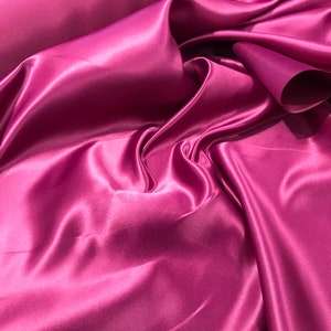 May include: A close-up of a smooth, silky fabric in a deep, rich magenta color. The fabric is draped and folded, showcasing its luxurious texture.