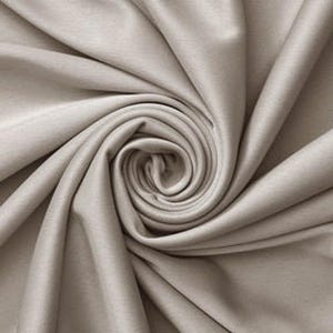 Könnte beinhalten: Ein einfarbiger, helltaupefarbener Stoff mit glatter, matter Textur, der in einer engen, zentralen Spirale angeordnet ist. Das Material weist weiche, fließende Falten auf, die von der Mitte ausstrahlen und tiefe Schatten und Lichter erzeugen.