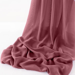May include: A flowing, draped fabric in a muted rose color. The material appears lightweight and sheer, with soft folds and subtle shadows. The fabric is likely used for apparel or home decor.