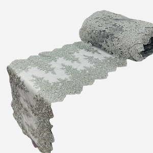 Puede incluir: Un ribete de encaje plateado con un borde festoneado. El encaje tiene un diseño floral y es perfecto para agregar un toque de elegancia a cualquier proyecto.