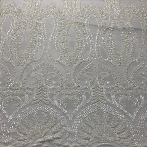 Puede incluir: Tela blanca con cuentas con un patrón de tipo paisley. La tela está hecha de lentejuelas y cuentas y tiene un diseño delicado e intrincado.