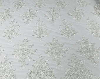 White floral design embroidery on a mesh lace with sequins and cord-sold by the yard.