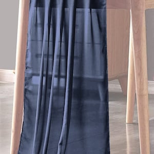 Puede incluir: Un camino de mesa azul oscuro hecho de tela transparente. El camino de mesa está drapeado sobre una mesa de madera y tiene una textura suave y fluida.