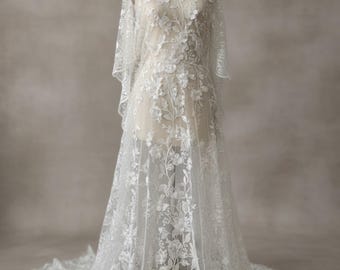 以下が含まれることがあります： 透け感のある生地全体に複雑な花の刺繍と葉の模様が施された、床までの長さの白いレースのガウン。この衣服は幅広で流れるような袖と、床に広がるトレーンが特徴で、細部まで作り込まれた刺繍が施されています。