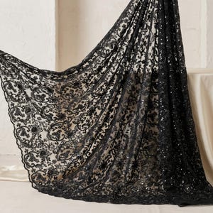 May include: Black lace fabric featuring a detailed floral and scroll design. The fabric is draped, showcasing the pattern and texture. The lace is adorned with sequins, providing a shimmering effect. Ideal for clothing and craft applications.