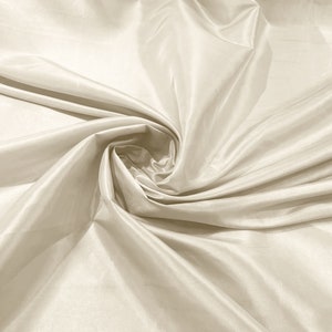 May include: A close-up of a smooth, ivory-colored fabric with soft, flowing folds. The fabric is draped and gathered in a swirling pattern, creating a luxurious and elegant look.