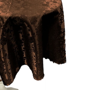 May include: A brown round tablecloth with a floral pattern. The tablecloth is draped over a white table base.