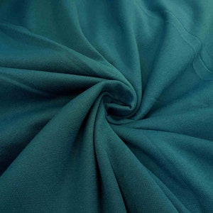 May include: Teal fabric with a textured surface. The fabric is folded and draped, showing its soft and smooth texture.