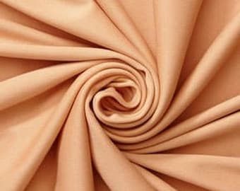May include: A solid light peach-coloured fabric with a smooth, matte texture. The material is gathered into a central spiral, creating deep, flowing folds and soft shadows that radiate outward from the centre point across the entire surface.