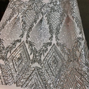 May include: Silver sequin fabric with a geometric pattern. The fabric has a white mesh backing.