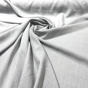 May include: A close-up of a light gray fabric with a subtle textured weave. The fabric is folded and draped, showcasing its soft and drapey texture.
