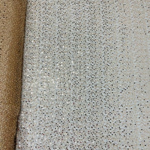 May include: A roll of gold sequin fabric. The fabric is covered in small, round sequins that catch the light. The sequins are a mix of gold and silver, creating a shimmering effect. The fabric is likely used for apparel or decorative purposes.