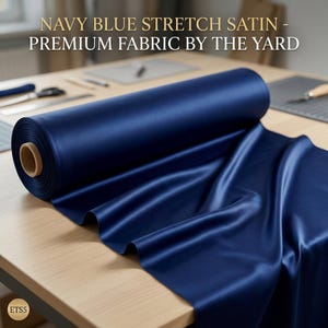 May include: A roll of navy blue stretch satin fabric, with the text "NAVY BLUE STRETCH SATIN - PREMIUM FABRIC BY THE YARD". The fabric is displayed on a wooden table, with a portion unrolled to show its sheen.