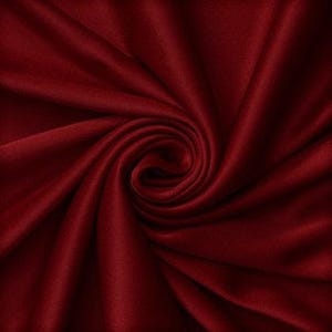 Könnte beinhalten: Ein tiefburgunderfarbener Stoff mit glatter, matter Textur, der in einem zentralen Spiralwirbelmuster angeordnet ist. Das Material weist weiche, fließende Falten auf, die von der Mitte ausstrahlen und subtile Schatten und Lichter erzeugen.