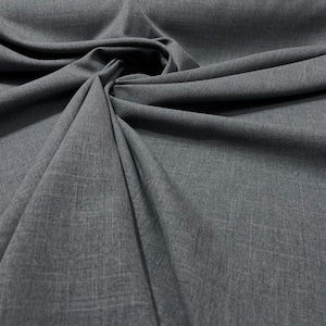 May include: Close-up of a gray textured fabric with a subtle woven pattern. The fabric is draped and folded, showcasing its soft and drapey texture.