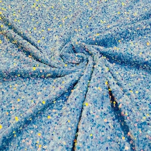 Peut inclure: Un tissu bleu clair recouvert d'une couche dense de petites paillettes rondes et irisées. Le matériau est rassemblé au centre, créant des plis et des ondulations doux qui soulignent le scintillement réfléchissant et multicolore des paillettes.