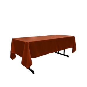 May include: A rust-colored rectangular tablecloth draped over a table with black metal legs.