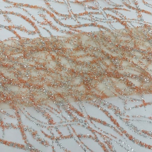 Pode incluir: Close-up de um tecido transparente com um padrão ondulado de lantejoulas prateadas e pêssego. O tecido é leve e arejado, e as lantejoulas são pequenas e delicadas.