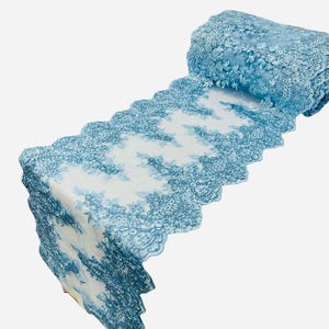 May include: A roll of light blue lace fabric with a floral design. The lace has a scalloped edge.