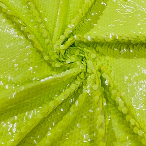 Puede incluir: Tela verde lima con un patrón de lentejuelas circulares. Las lentejuelas se superponen y crean un aspecto texturizado.