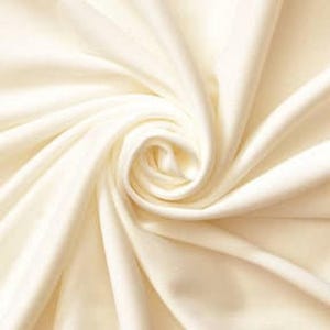 Könnte beinhalten: Ein glatter, cremeweißer Stoff mit einer glänzenden, reflektierenden Oberfläche. Das Material ist in einer engen, zentralen Spirale angeordnet, wodurch tiefe, fließende Falten und weiche Schatten entstehen, die den Glanz und die Textur betonen.