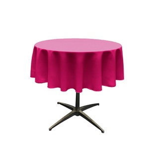 Puede incluir: Un mantel redondo de color rosa con un borde festoneado, drapeado sobre una mesa redonda con una base de cuatro patas.