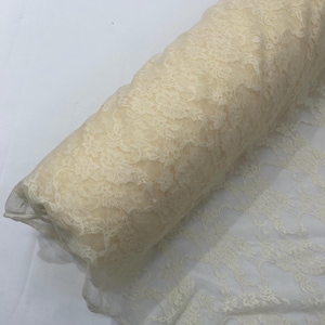 以下が含まれることがあります： 繊細で複雑な花柄が特徴のクリーム色のレース生地のロール。素材は半透明で軽量であり、レースのデザインは細かいメッシュベースに織り込まれています。生地は円筒形のボルト状にしっかりと巻き付けられています。
