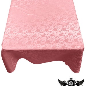 May include: A light pink rectangular tablecloth with a floral pattern. The fabric has a subtle sheen and drapes over a table. The tablecloth is made of fabric and foam. The logo for New Creations Fabric & Foam is in the bottom right corner.