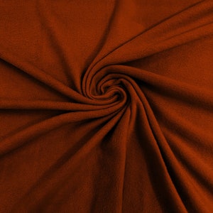 May include: A close-up of a rust-colored fabric with a soft, fuzzy texture. The fabric is folded and draped in a spiral pattern, creating a visually appealing and tactile image.