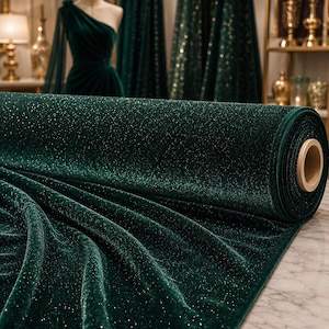 May include: A roll of emerald green velvet fabric with a subtle sparkle. The fabric is draped and rolled, showcasing its texture and sheen. In the background, a dress form displays a matching velvet gown.