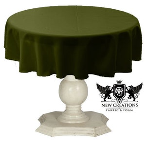 Può includere: Una tovaglia rotonda di colore verde oliva drappeggiata su un tavolo a piedistallo bianco. Il tavolo ha un piano rotondo e una base con un design decorativo e scanalato. La tovaglia è realizzata in un tessuto morbido e liscio.