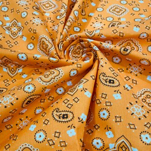 Pode incluir: Tecido laranja com um padrão paisley branco e preto. O tecido está dobrado e tem uma superfície texturizada.