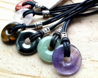 May include: Seven gemstone donut pendants on black cords with silver clasps. The stones are amethyst, green aventurine, black obsidian, tiger's eye, rose quartz, and clear quartz.