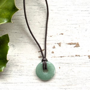 May include: A green jade stone donut pendant on a brown leather cord necklace.