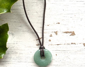 May include: A green jade stone donut pendant on a brown leather cord necklace.