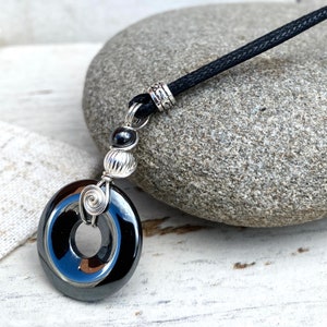 May include: A black hematite pendant necklace with a silver wire wrapped around the stone. The pendant is attached to a black cord with a silver bead.