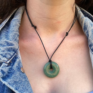 Könnte beinhalten: Eine Halskette mit einem grünen Jade-Donut-Anhänger an einem schwarzen Lederband.