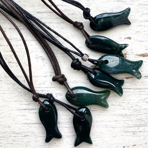May include: A set of seven green agate fish pendants on brown leather cords. The pendants are all different shapes and sizes, and they are all polished to a smooth finish.