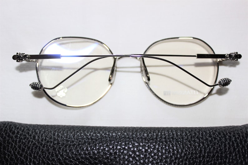 May include: Silver-toned round eyeglasses with a black leather case. The glasses have a thin metal frame and a delicate design on the temples.