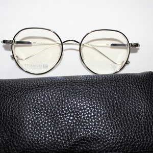 May include: Silver-rimmed round eyeglasses with clear lenses and a black leather glasses case. The glasses have the text "Titanium" printed on the frame.