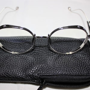 May include: Silver round-framed glasses with a black leather case. The glasses have a textured metal frame and clear lenses.